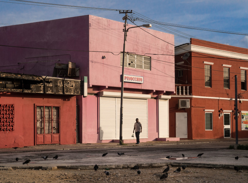 Ben Asen Personal Work Photo: Color photo of a man walking down a street in Aruba in front of a building with a sign that reads Pinocchio