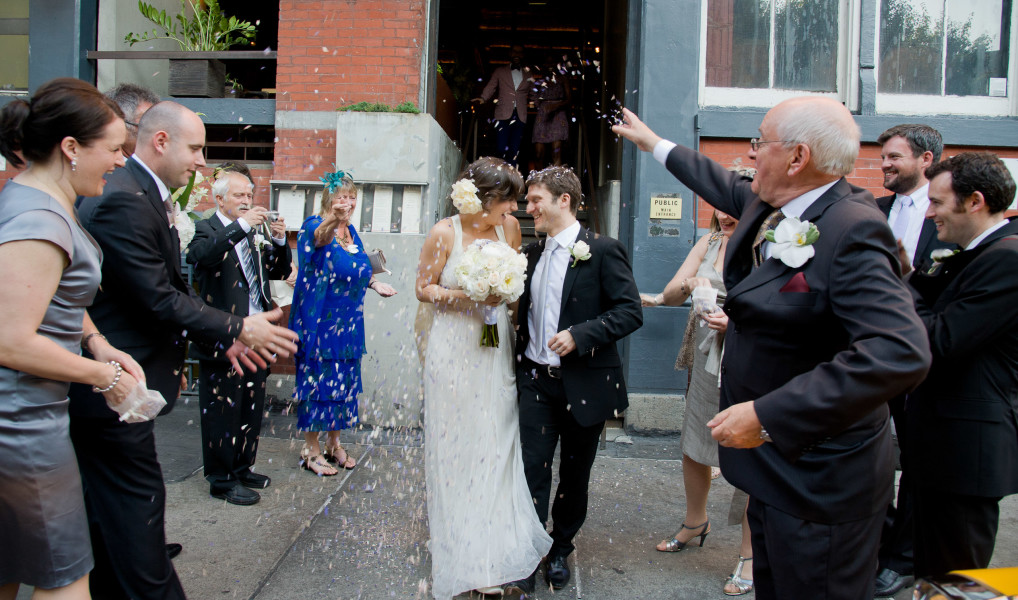 Ben Asen Celebrations Photo: Color photo of bride and groom kissing while having rice being thrown at them by family and friends