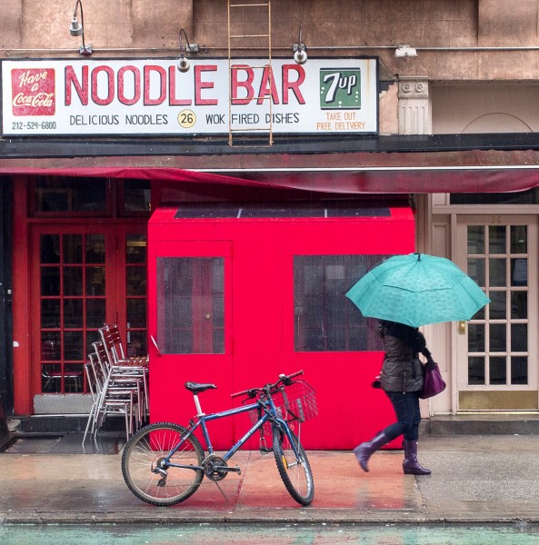 Ben Asen Personal Work Photo: color photo of a woman with an umbrella walking past the Noodle Bar in Greenwich Village, New York City